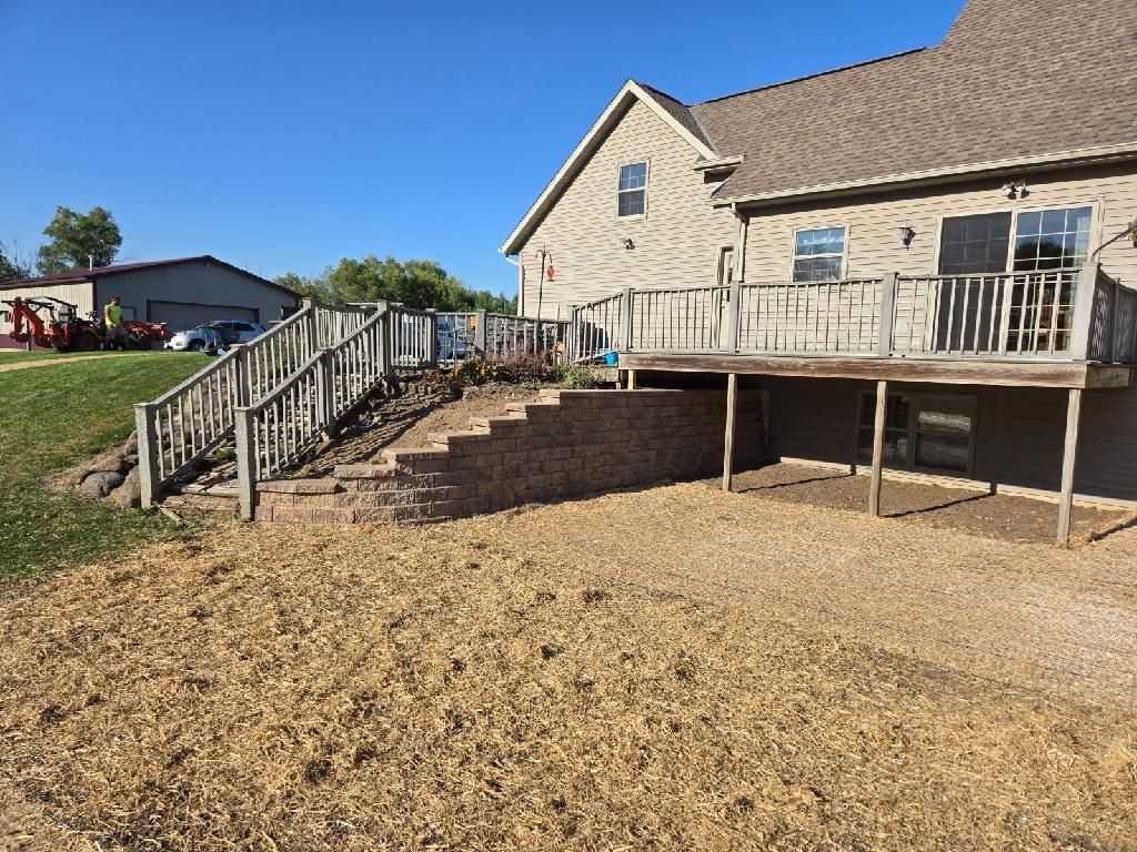 After: new engineered block retaining wall with a clean graded base beneath the deck